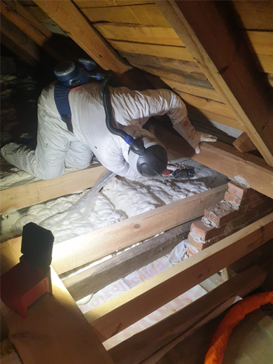 Pracownik docieplający poddasze pianą PUR